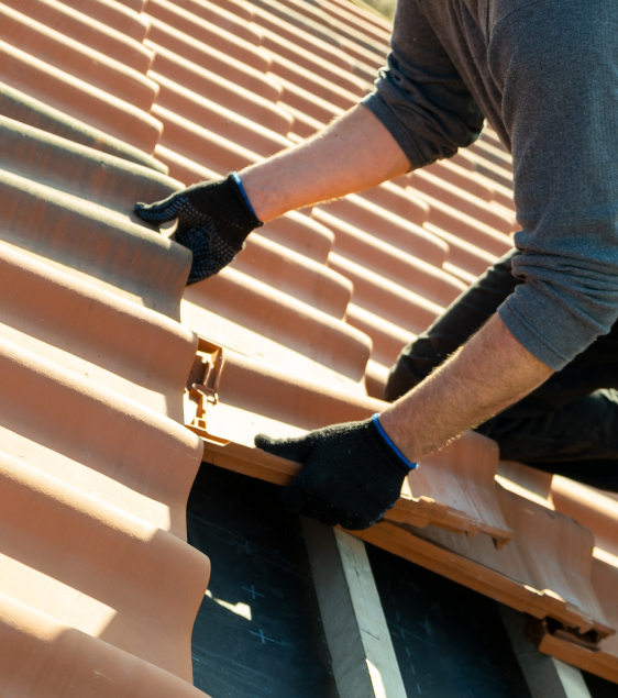 Class 4 Upgrade Person wearing gloves installing or repairing terracotta roof tiles on a sloped roof as part of roofing restoration in Colorado Springs.