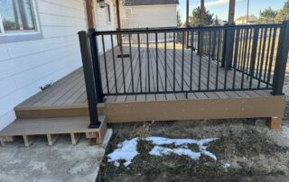 CPS Roofing Colorado Springs A brown composite deck with black railing, attached to a restored white house in Colorado Springs, overlooks patchy snow and grass.