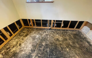 Room with exposed wall studs, stripped flooring, and window—interior repairs underway after Colorado Springs roof restoration.