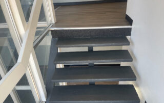 Floating black metal stairs with glass railing ascend to a wood-floor landing, part of a Colorado Springs home restoration project.