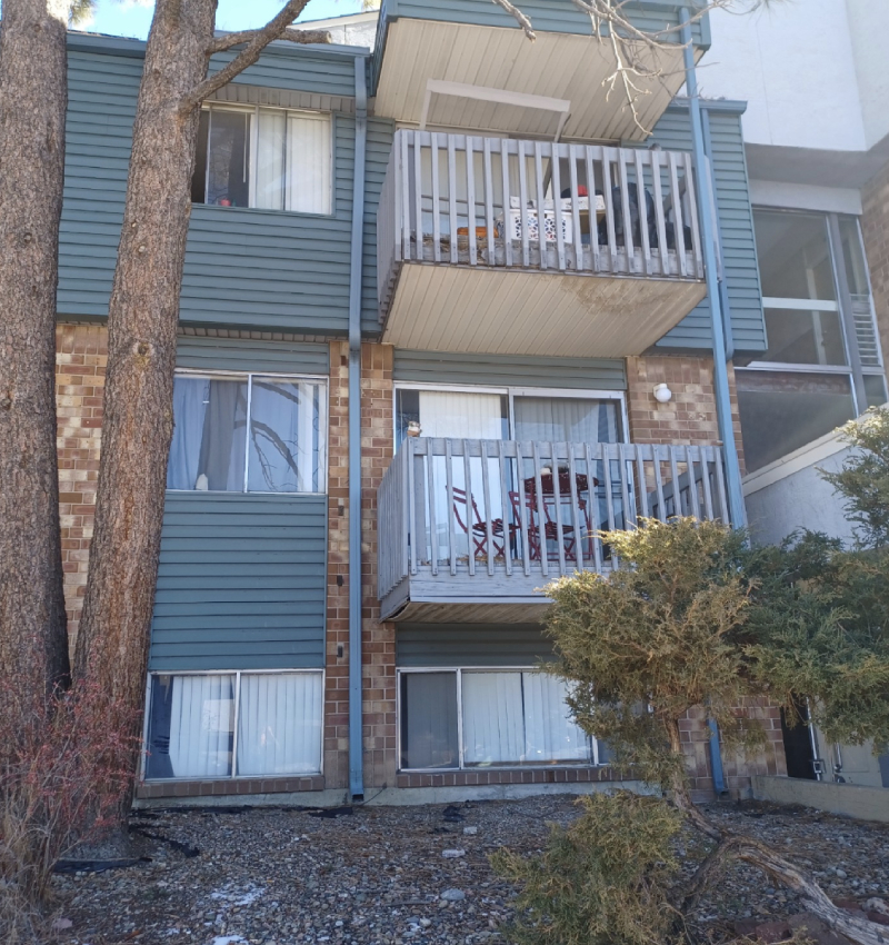 Three-story apartment with brick and blue siding, balconies, leafless trees, and newly restored roofing in Colorado Springs.