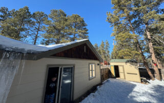 A person stands in a beige doorway; snow and a large icicle on the roof hint at the need for roofing restoration in Colorado Springs.