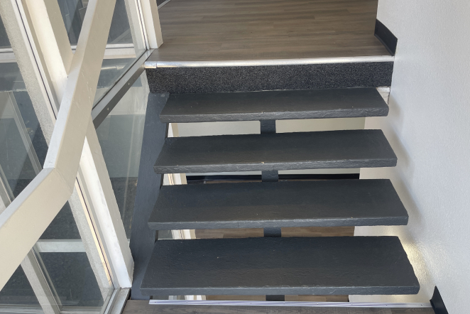 Interior Restoration — drywall, flooring, and more Floating black stairs with no risers, metal supports, and a glass window showcasing a Colorado Springs roof restoration outside.