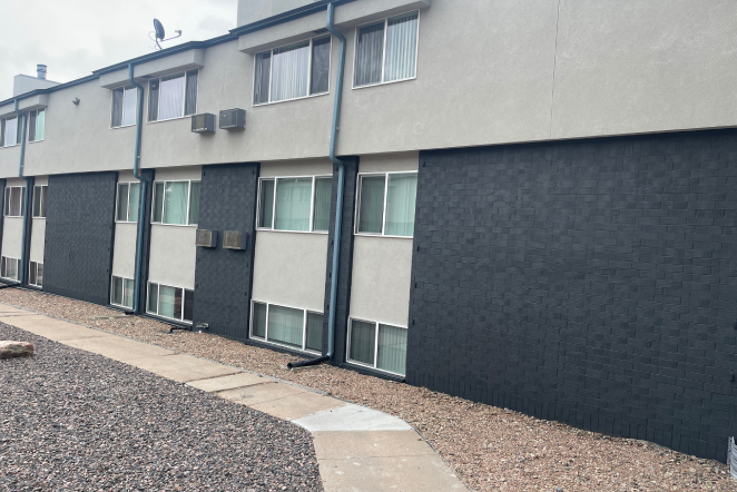 A two-story apartment in Colorado Springs with gray and black exterior, new roofing, multiple windows, and gravel landscaping.