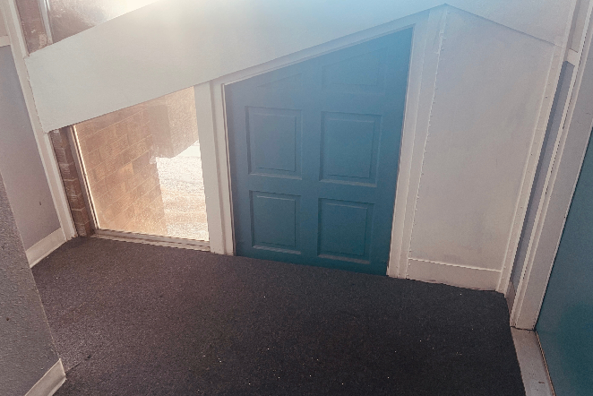 A small blue door with four panels in a slanted wall, beside a tall window, highlights Colorado Springs home restoration quality.