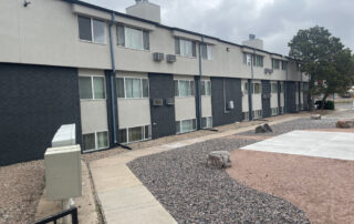 colorado springs roofing contractor A three-story apartment in Colorado Springs with a restored roof, gray/black exterior, landscaped yard, under a cloudy sky.