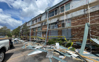 Debris and construction materials on the ground beside a building in Colorado Springs, with scaffolding and workers restoring the exterior roof.
