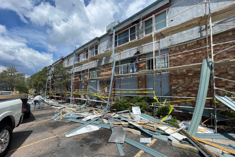 full-service roofing contractor Debris and construction materials on the ground beside a building in Colorado Springs, with scaffolding and workers restoring the exterior roof.