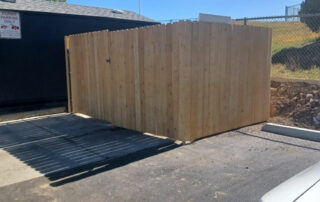 A wooden enclosure with a gate stands by a parking lot, next to a building—ideal for Colorado Springs roofing restoration needs.