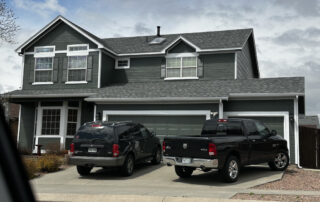 roofing contractor in colorado springs Two black pickup trucks, likely for a Colorado Springs roofing or exterior restoration team, are parked at a two-story gray house.
